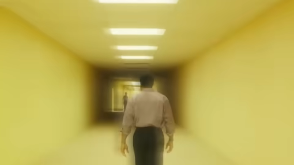 Un homme seul dans un couloir de bureaux jaune.